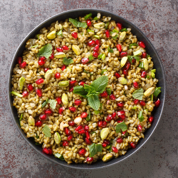 Delicious vegetarian freekeh with pomegranate, nuts and herbs close-up in a plate on the table. horizontal top view from above