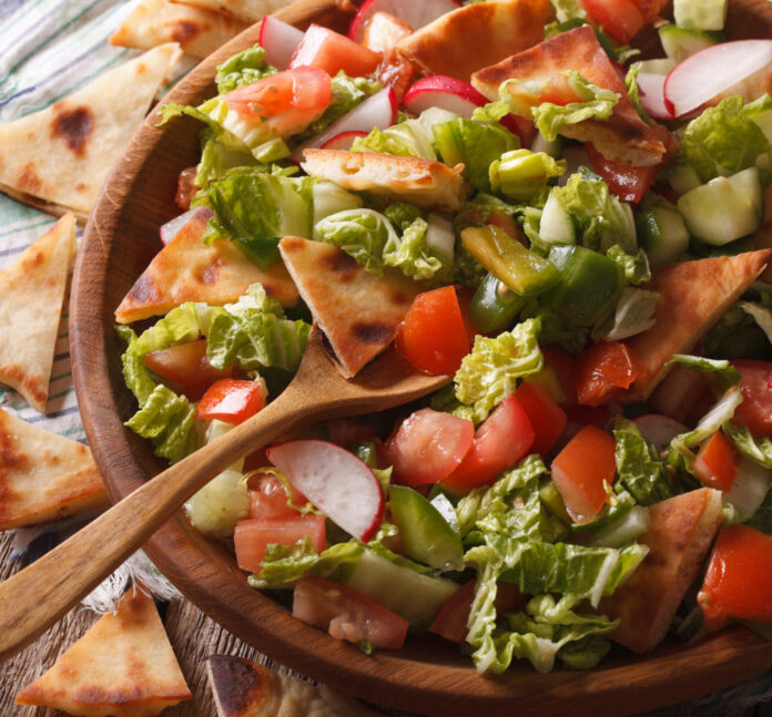 Fattoush salad with pita bread and vegetables close up in a wooden bowl. horizontal